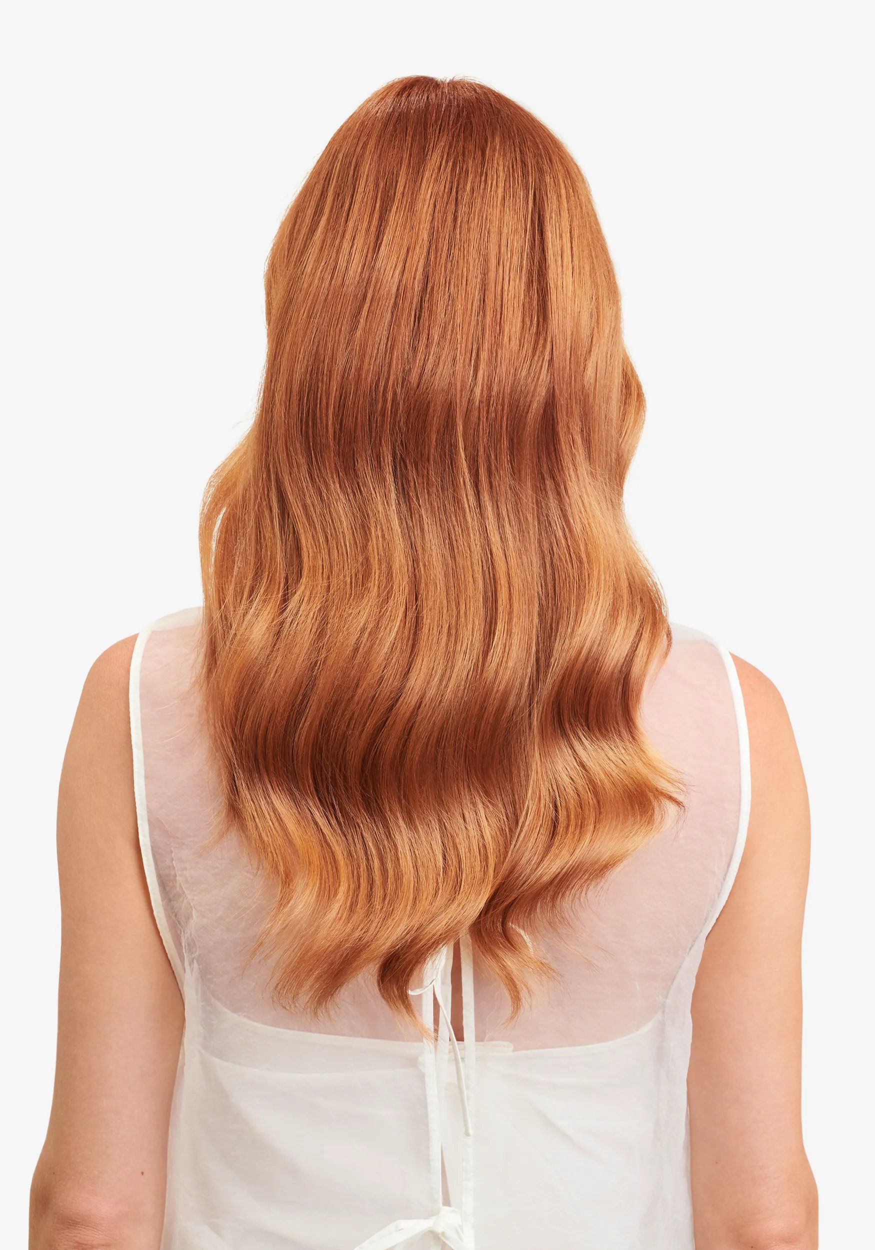 Back view of a woman with long, wavy strawberry blonde hair wearing a sheer white top against a white background.