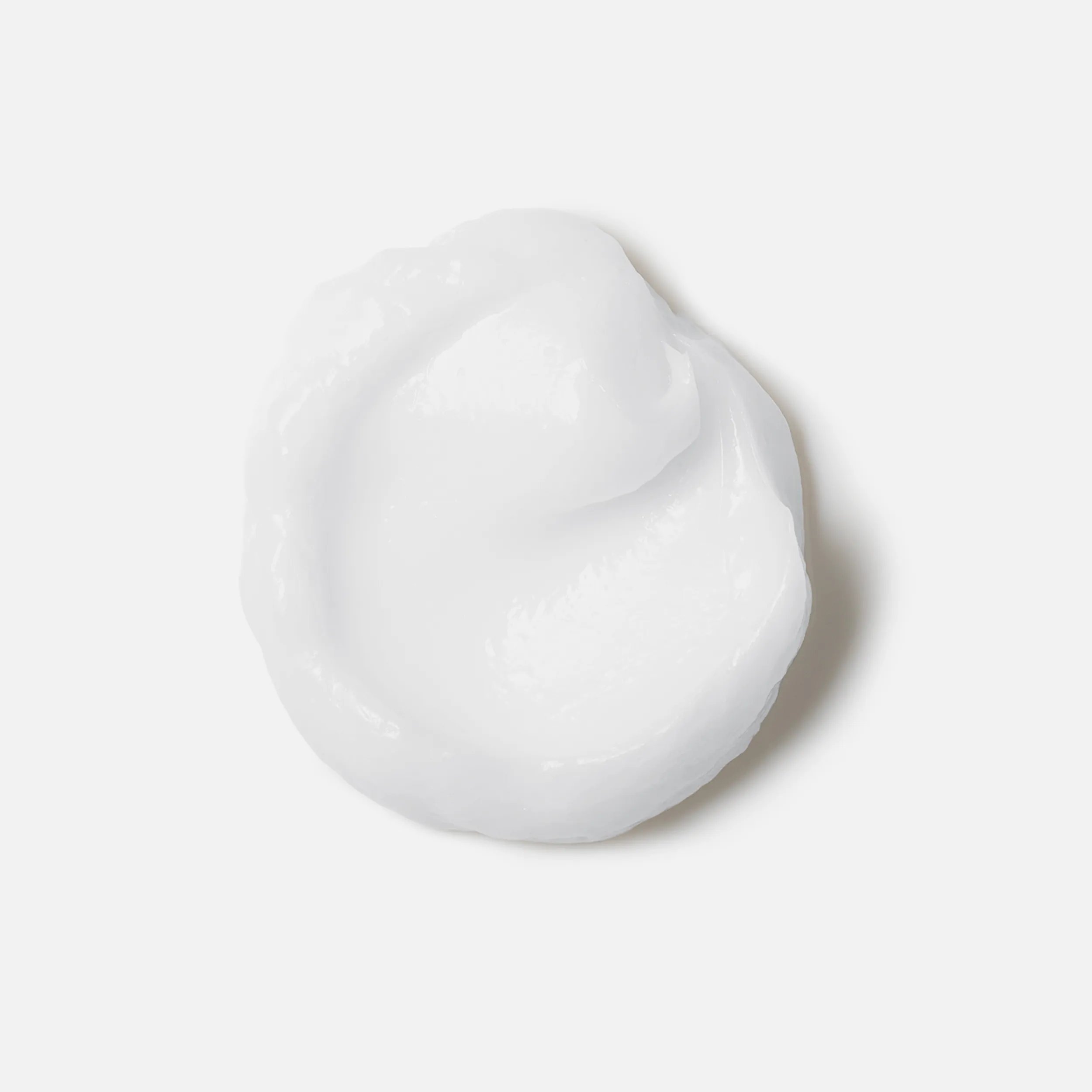 Photographie en gros plan d'une tache circulaire du produit Invigo Brilliance sur un fond blanc, avec un texte indiquant « bouclier antioxydant, aide à contrôler le processus d'oxydation après la coloration" et "purificateur de métaux, protège contre les métaux nocifs dans l'eau ».