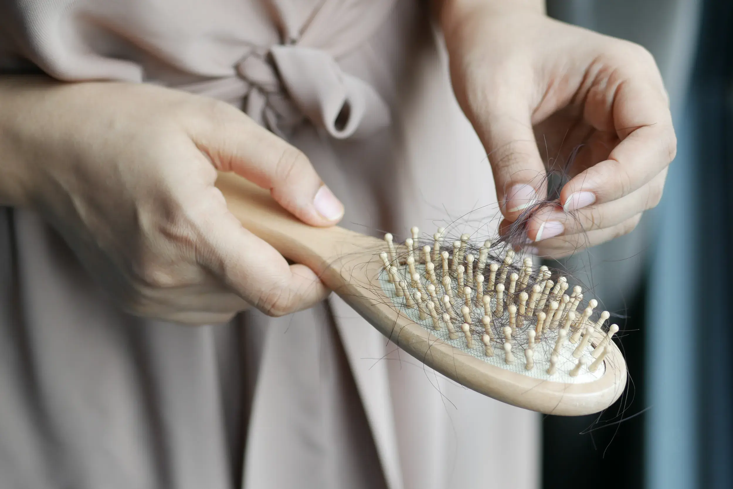 A woman’s hands hold out a wooden hairbrush as she pulls dark hair from its bristles.