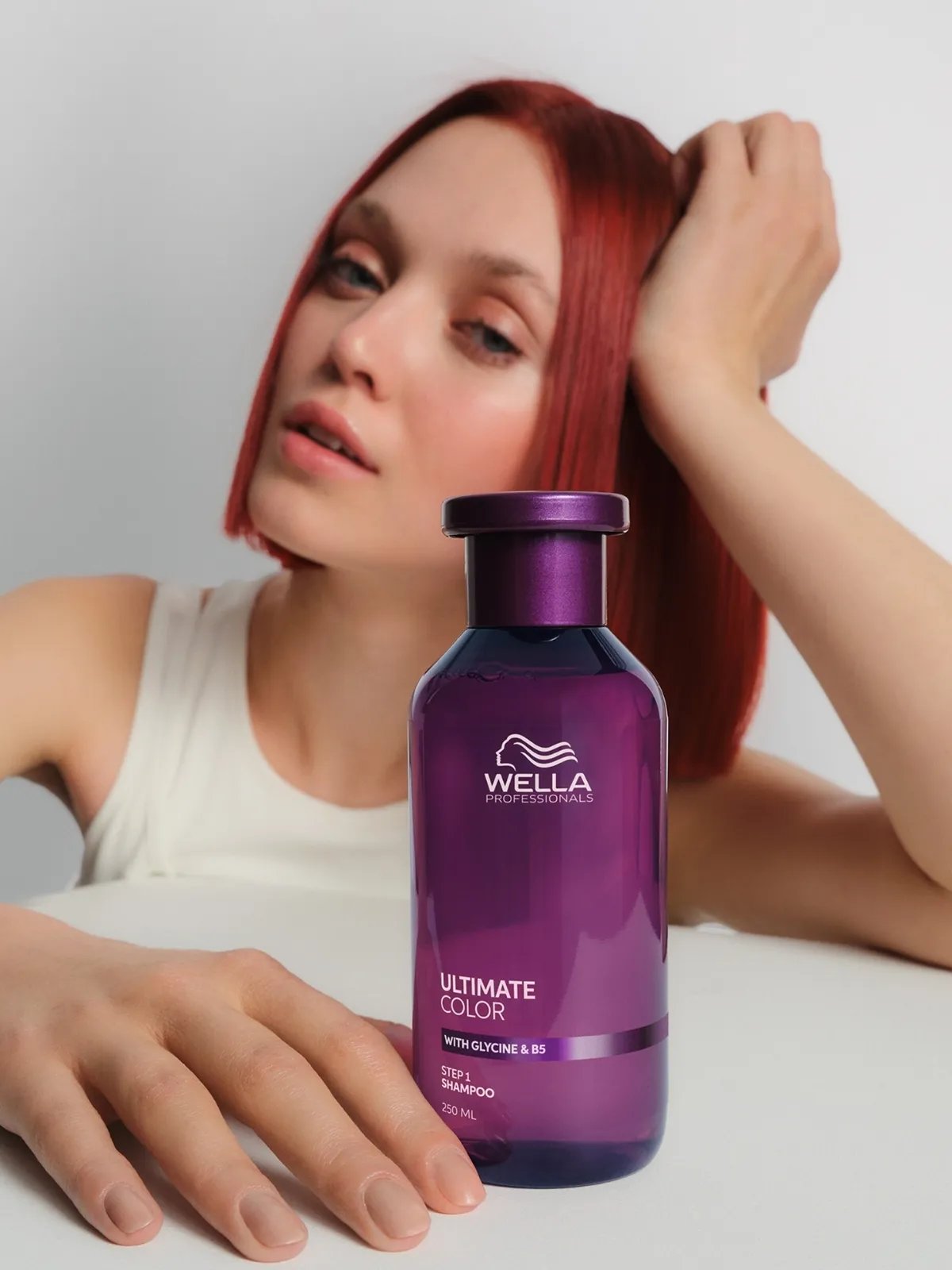 Model with bright red, straight hair holds a bottle of ULTIMATE COLOR Sulfate-Free Shampoo.