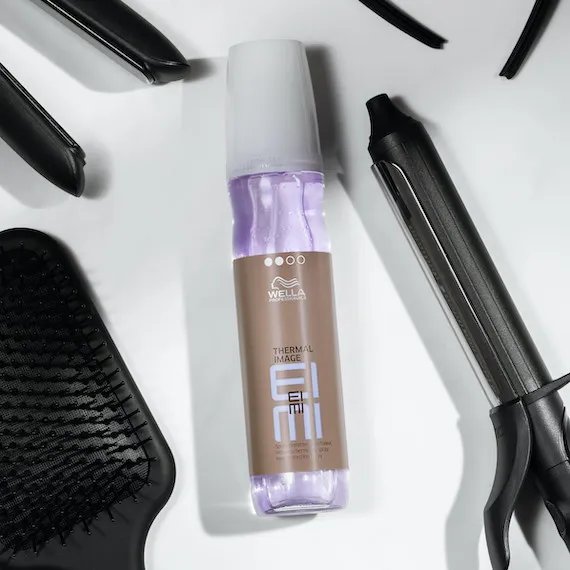 Eine Flasche EIMI Thermal Mist Hitzeschutzspray, umgeben von Stylingutensilien. 