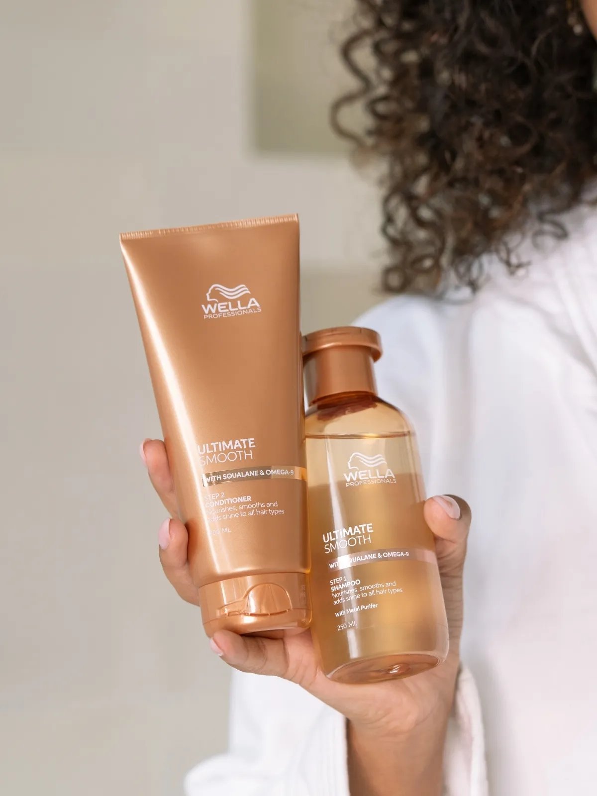 Model holds up ULTIMATE SMOOTH Conditioner and ULTIMATE SMOOTH Shampoo. 