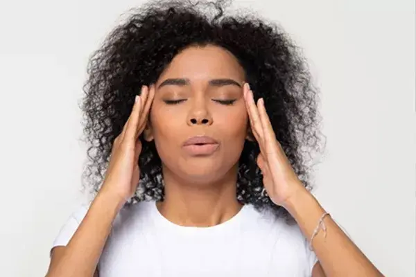 mixed race woman with curly hair with fingers on forehead temples taking a breath