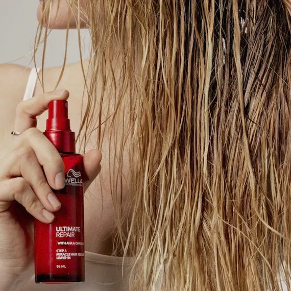 Model mists ULTIMATE REPAIR Miracle Hair Rescue through damp hair.