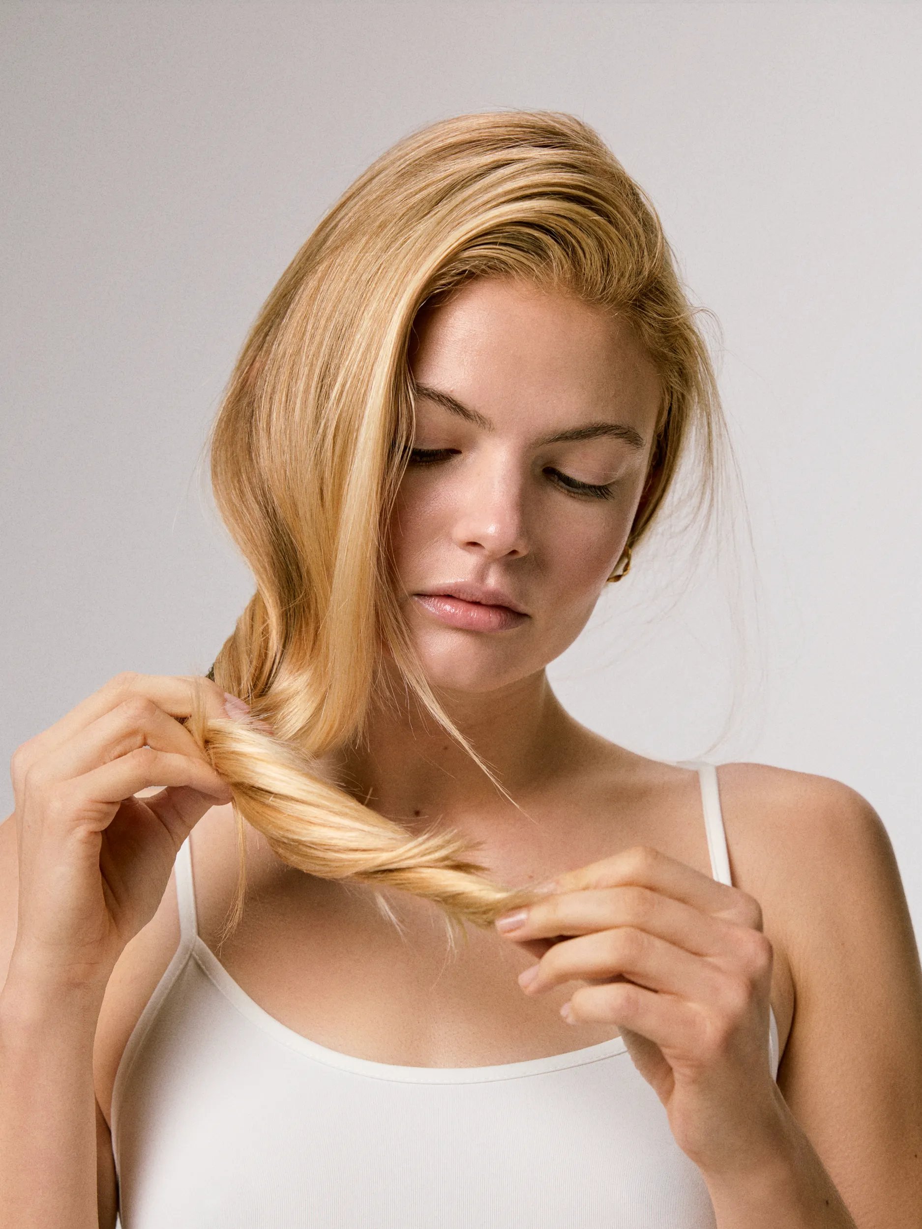 Model with long blonde hair looks at her split ends