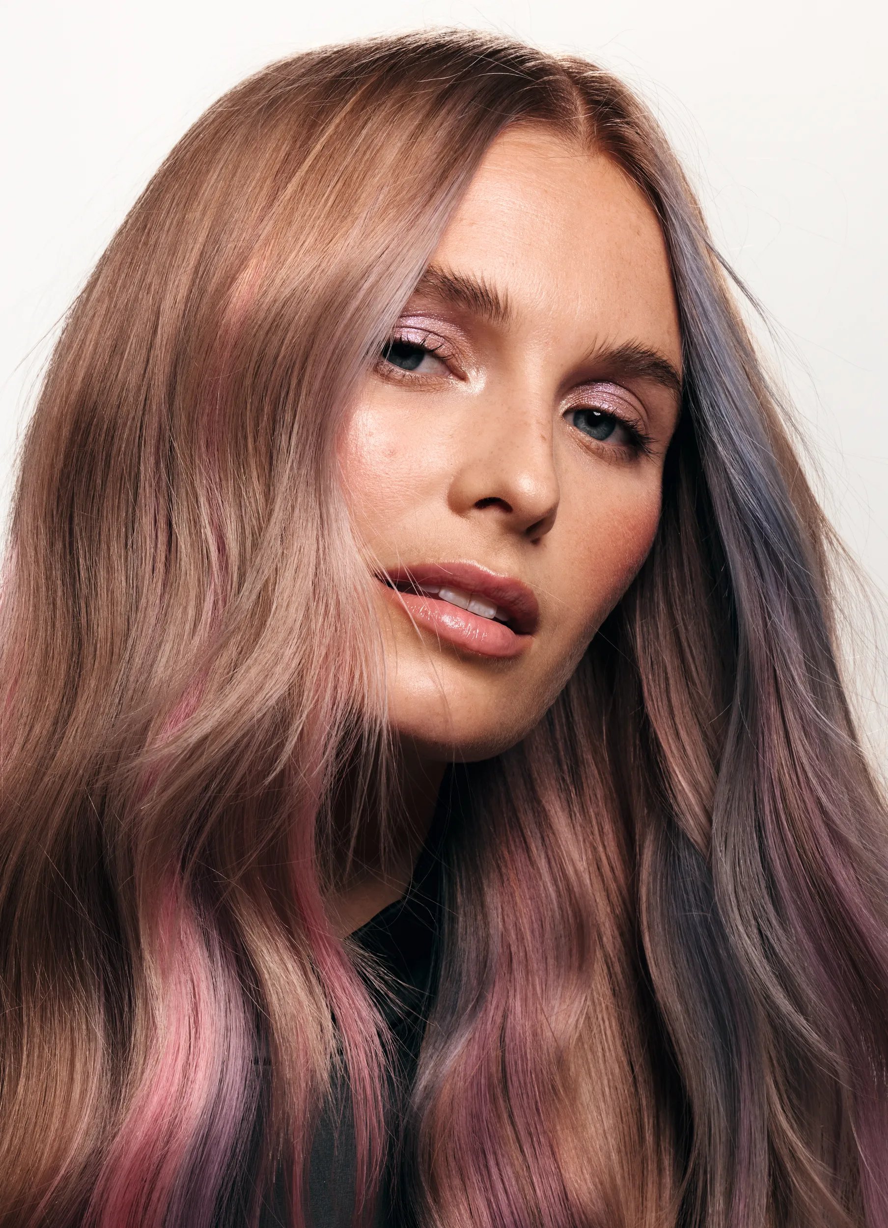 Model with long pastel balayage hair featuring pink, lavender, and silver tones, styled in loose waves to showcase Wella Professionals Surreal Color. 
