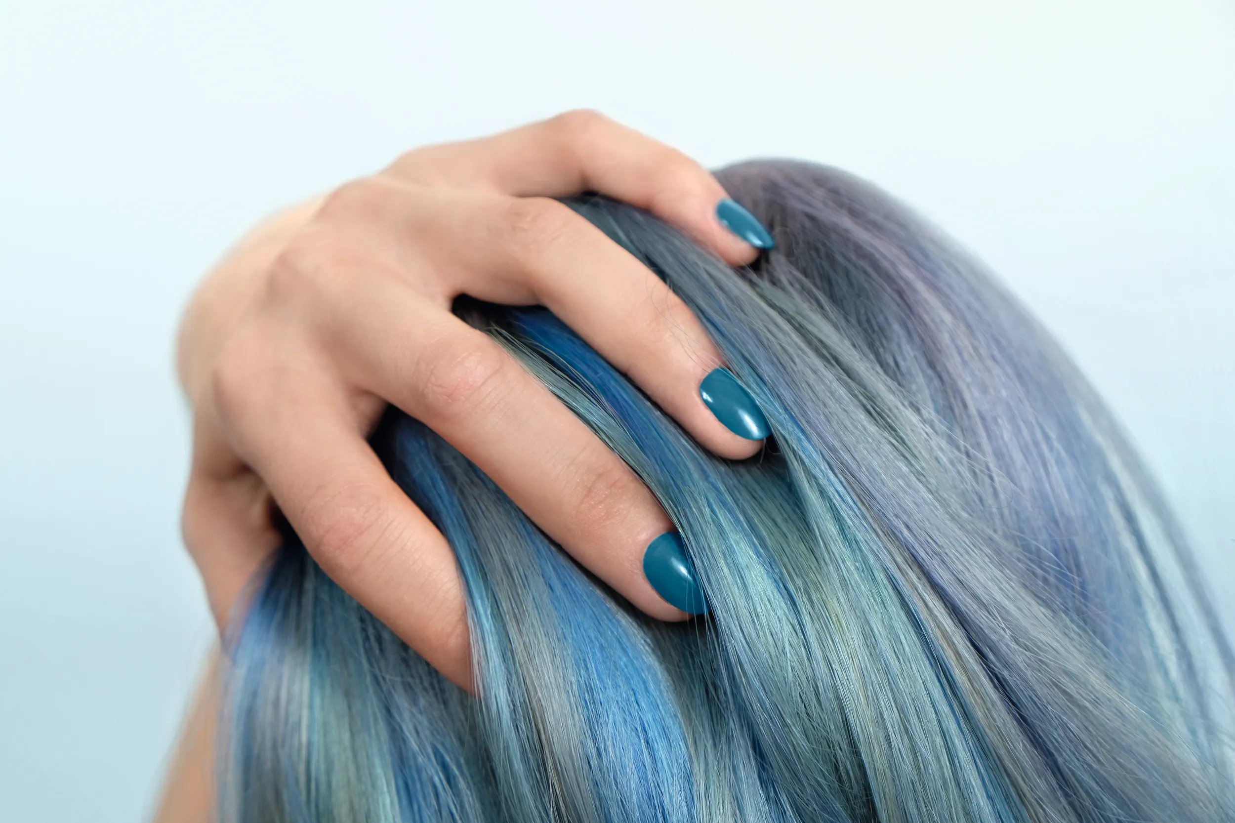 A hand with teal nail polish rests on multi-toned blue and gray hair.
