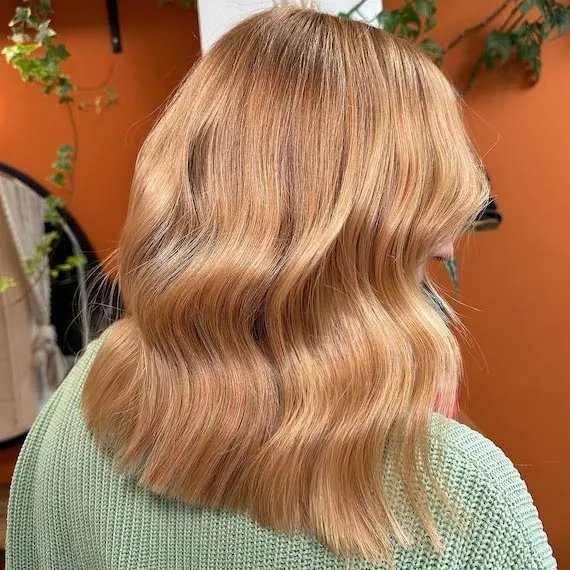 Model with glowy golden blonde hair, styled in a loose, polished wave