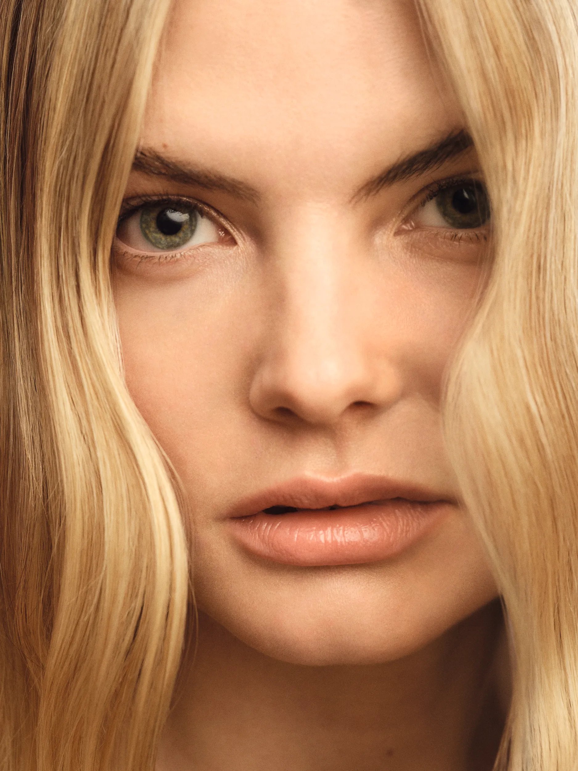Model with a mid length, wavy blonde balayage looks to the camera.
