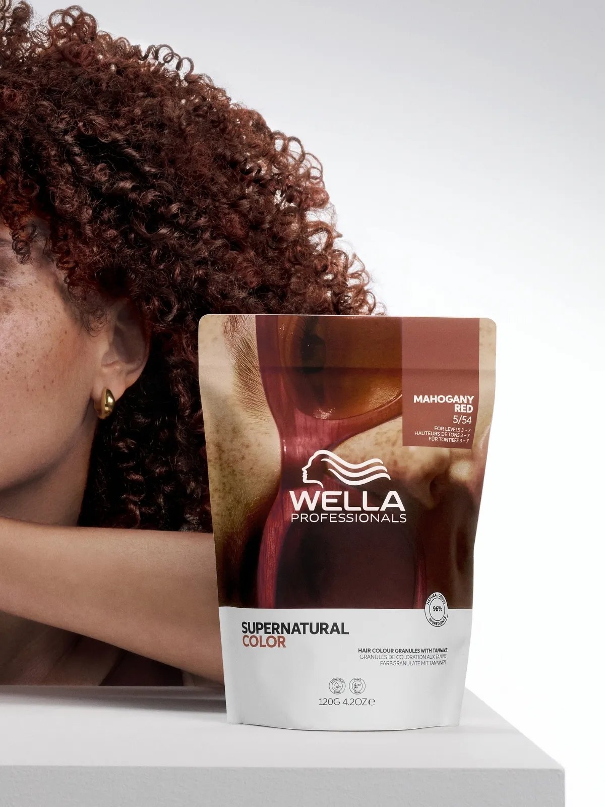 Mahogany-haired model poses next to a pouch of Supernatural Color in Mahogany Red.