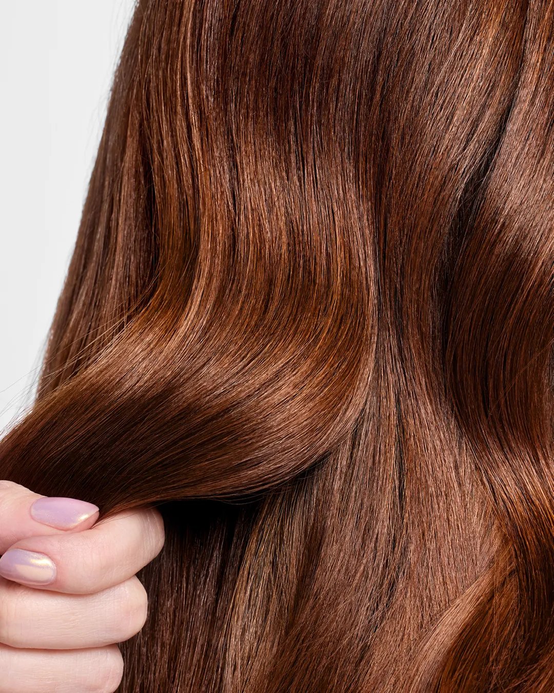 Close-up of smooth, shiny brown hair being gently held by a hand with pastel-colored nails.