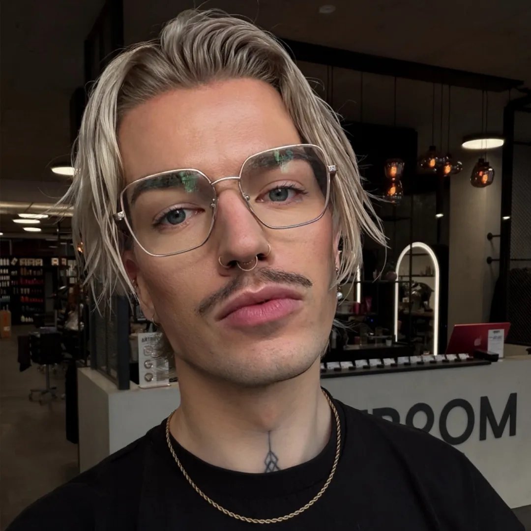 Blonder, junger Mann, der selbstsicher von oben in die Kamera herunterschaut.