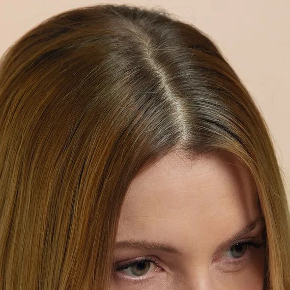 Close-up of model’s gray roots against light brown hair.