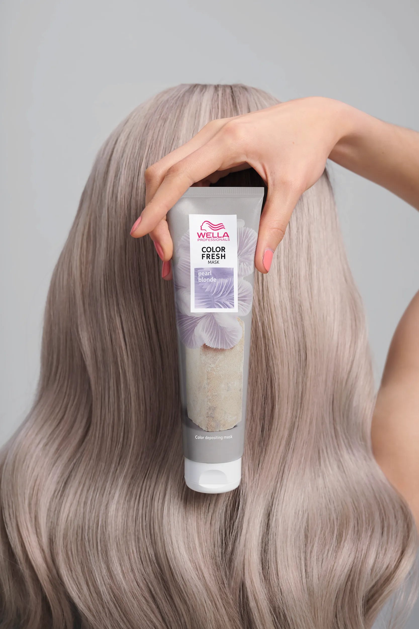 Person holds a bottle of Color Fresh by Wella Professionals on top of their curly, light brown hair