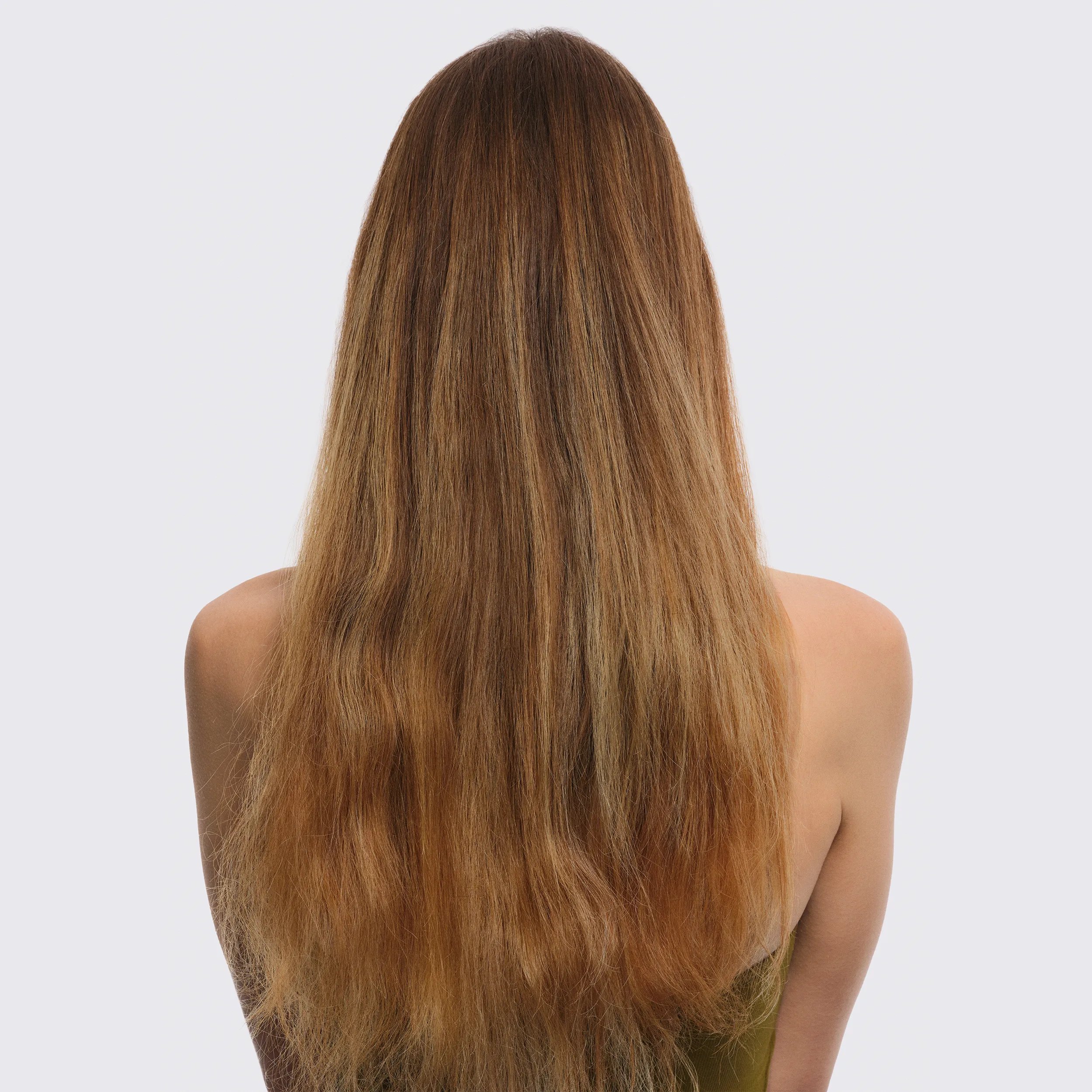 Εικόνα μοντέλου με γυρισμένη την πλάτη μπροστά από λευκό φόντο. Τα μαλλιά του μοντέλου είναι μακρυά με ξανθούς και κόκκινους τόνους. Φοράει ένα πράσινο τοπ.