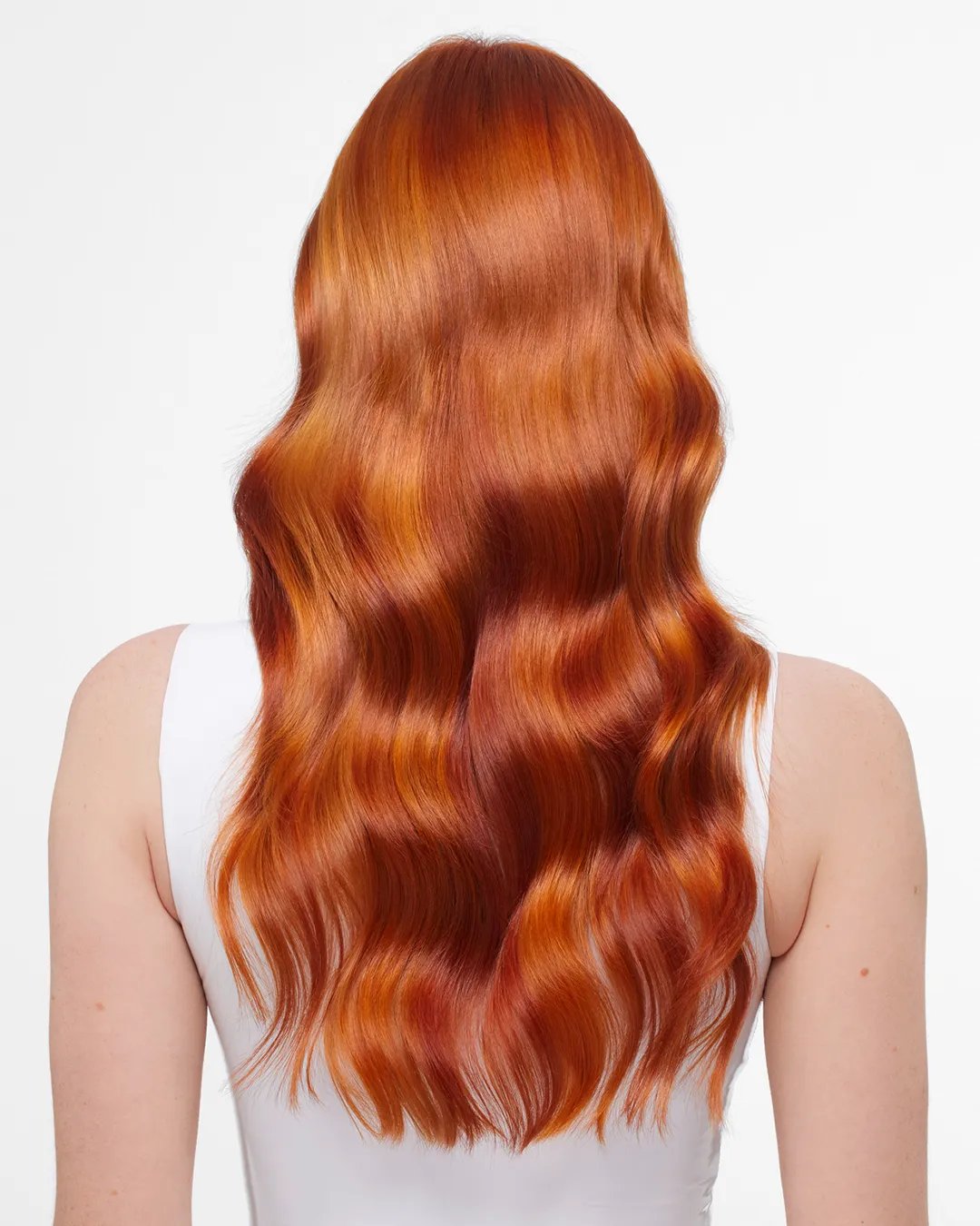 Back view of a woman with long, wavy copper-colored hair, wearing a white tank top against a white background.