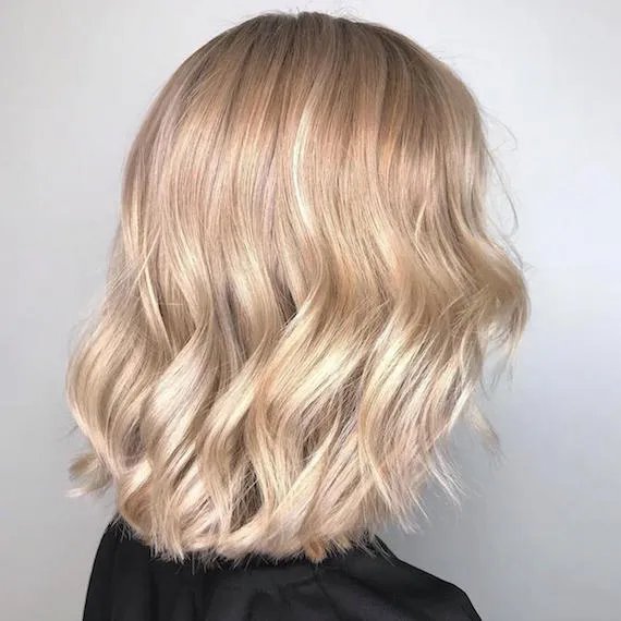 Side profile of woman with blonde balayage bob styled in loose waves, created using Wella Professionals.