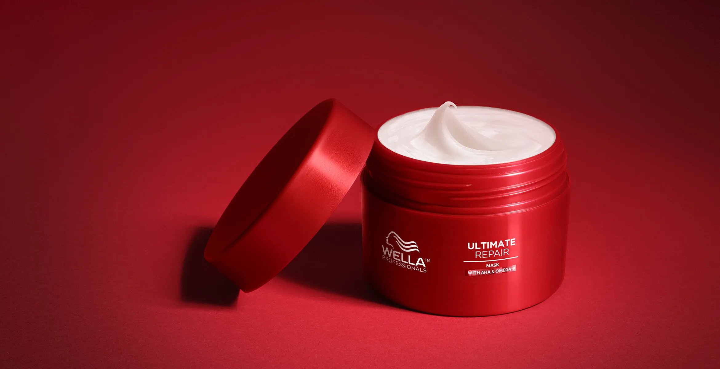 An open jar of ULTIMATE REPAIR Mask on a red surface.