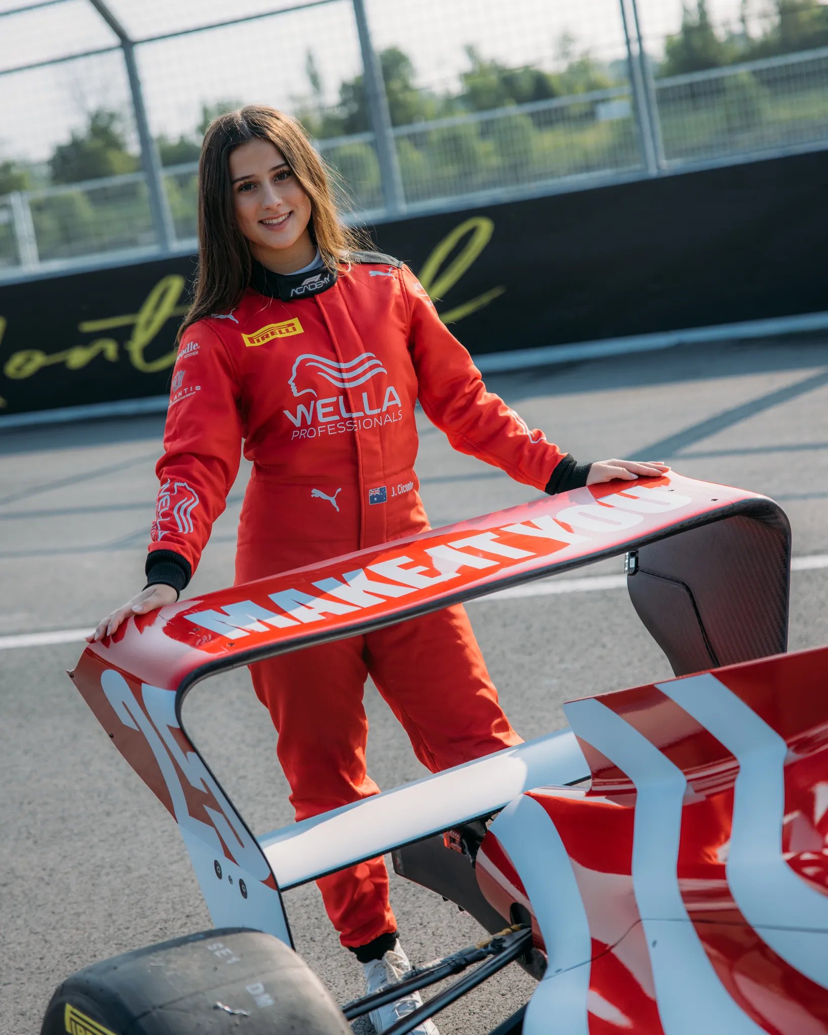 Joanne Ciconte from F1 Academy wearing a red Wella Professionals suit and car