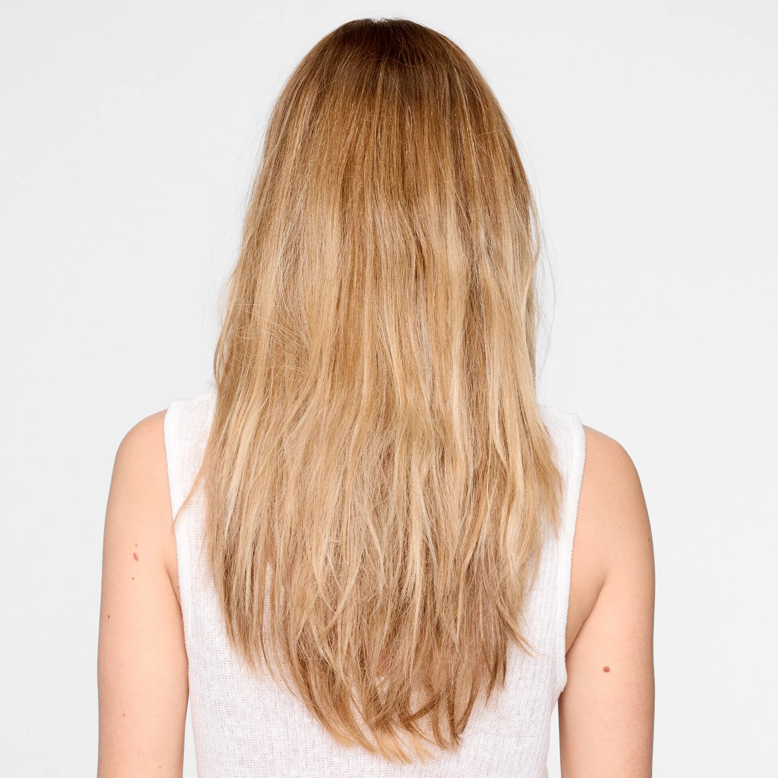 Back view of a model against a light gray background. The model's hair is blonde and frizzy, they are wearing all white. 