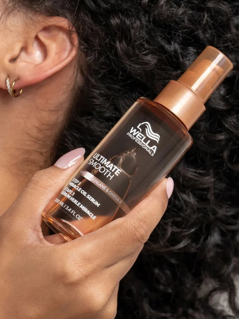 Model with dark brown hair holds a bottle of ULTIMATE SMOOTH Miracle Oil Serum.