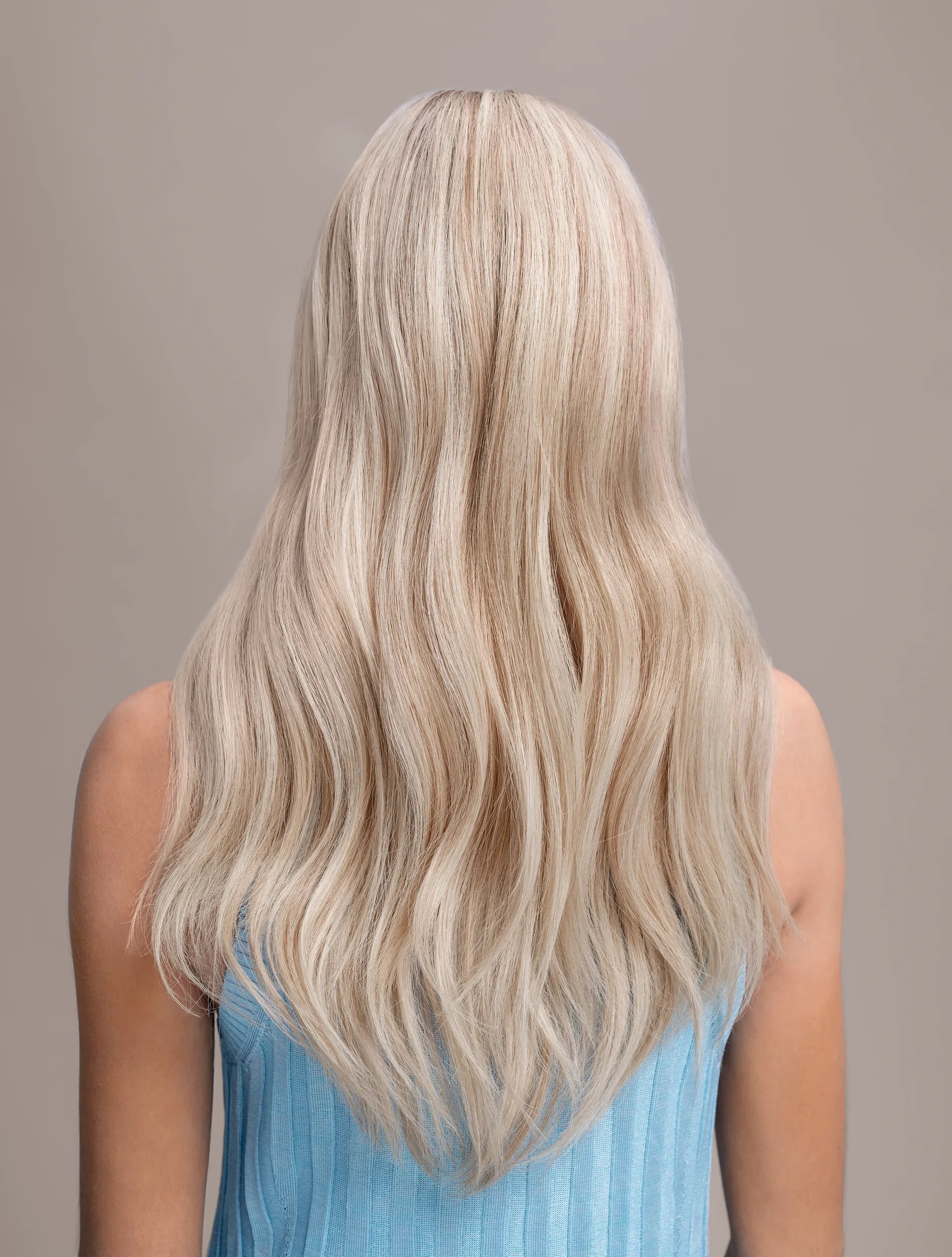 Back view of woman with long pearl hair, wearing a blue tshirt posing against a neutral background.