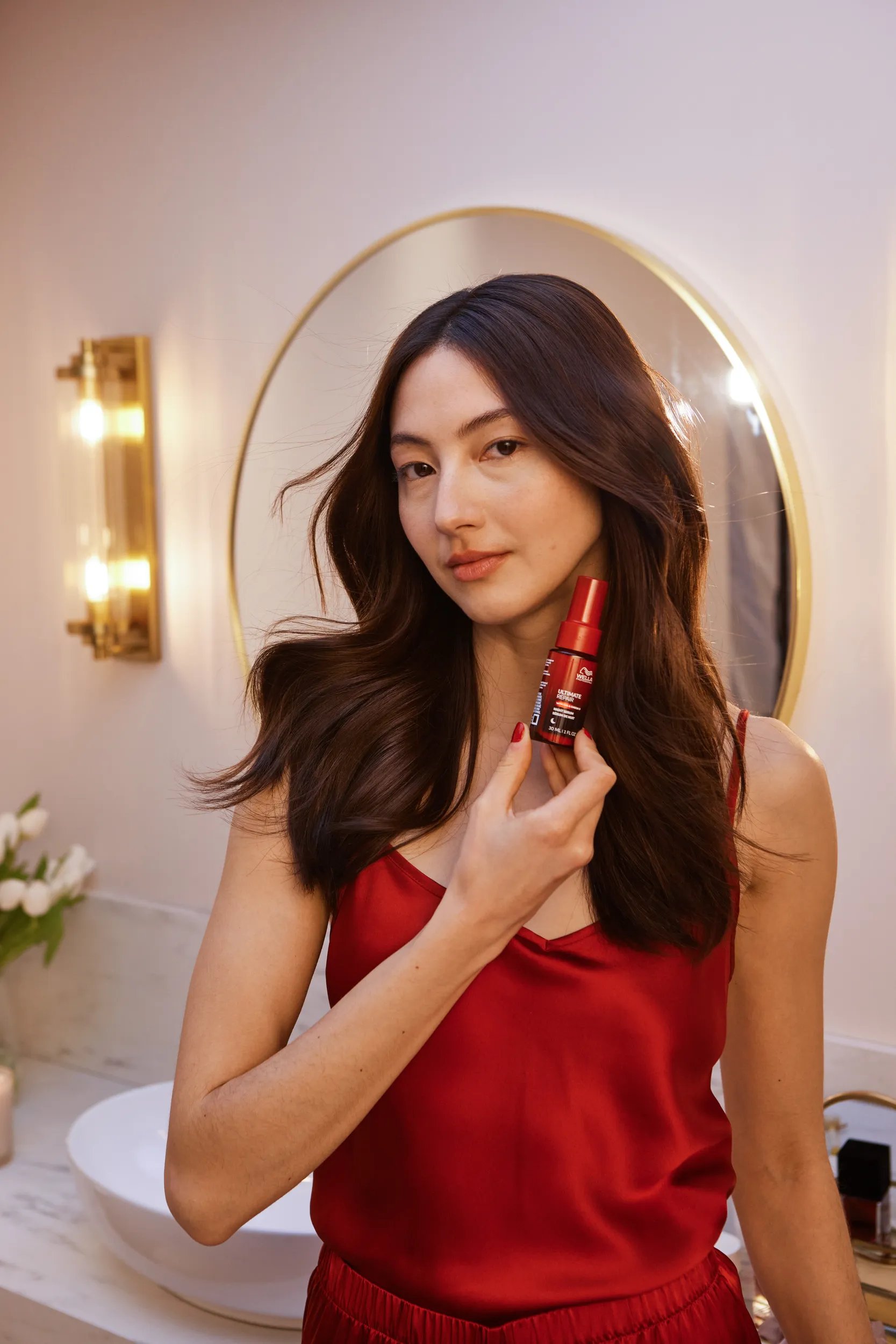 Model with long, dark hair styled in loose waves holds up ULTIMATE REPAIR Night Serum.