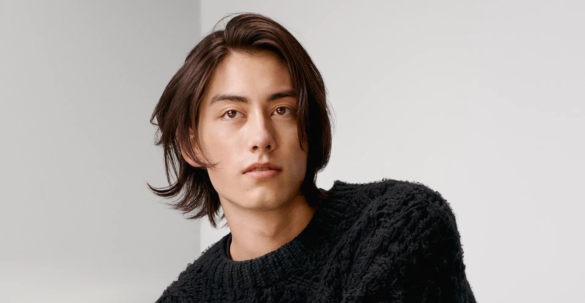 Modèle aux cheveux bruns courts, assis sur un lit et vêtu de noir  