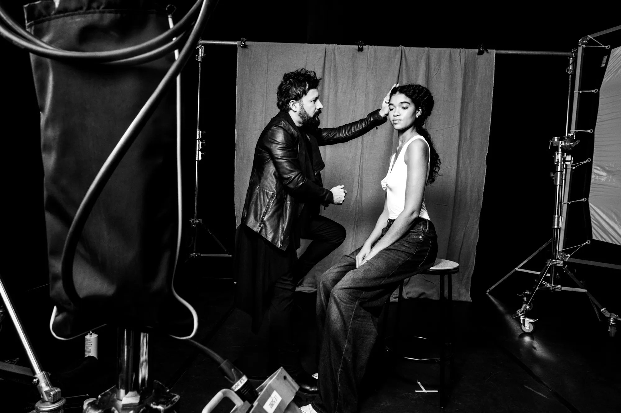 Black and white photo of a hairstylist adjusting a seated model’s hair on a photoshoot set