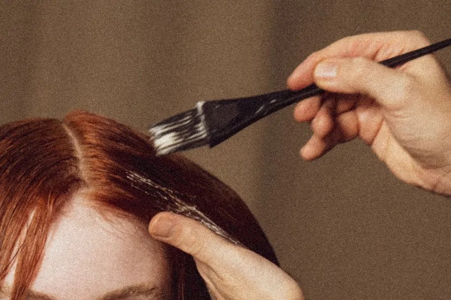 Nahaufnahme eines Stylists, der Farbe auf das kastanienbraune Haar eines Models aufträgt. 