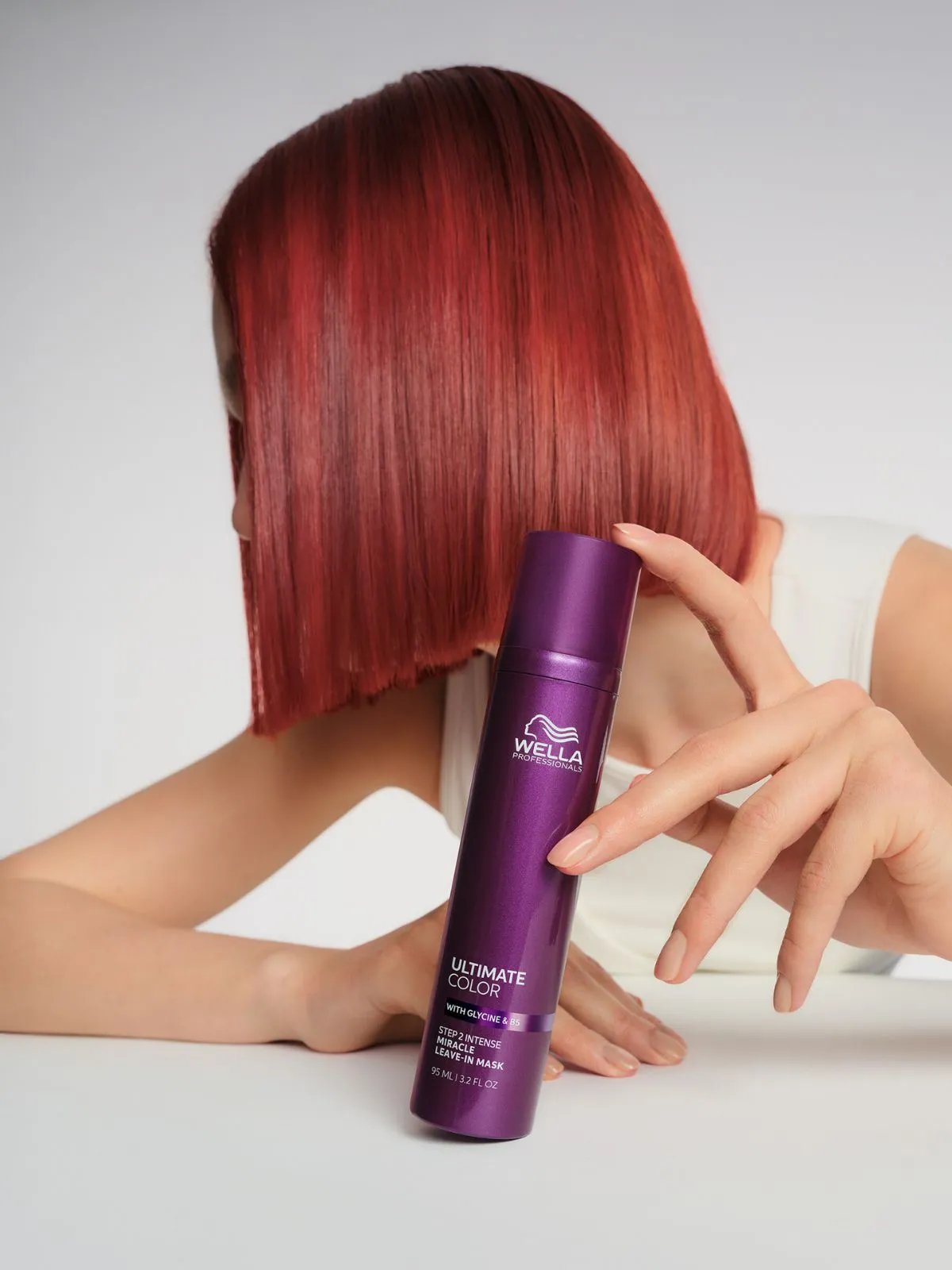Model with bright red bob haircut holds a bottle of ULTIMATE COLOR Miracle Leave-In Mask. 
