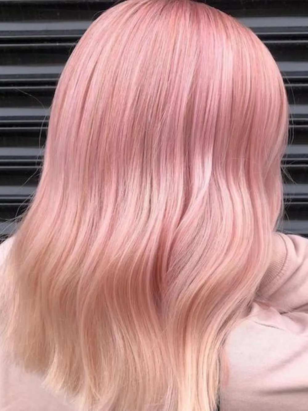 Back view of a model with wavy pink ombré hair and lighter ends.