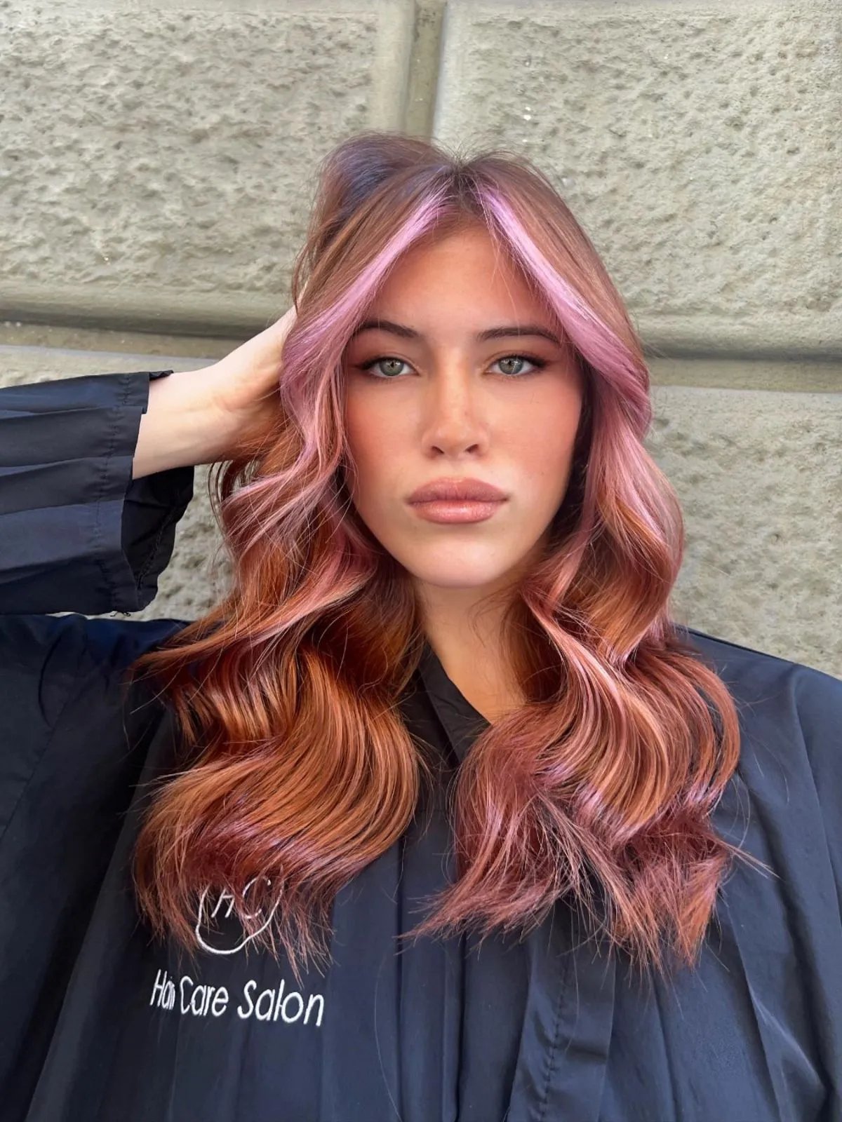 Model with long, wavy, rose gold hair featuring pastel pink face-framing highlights. 