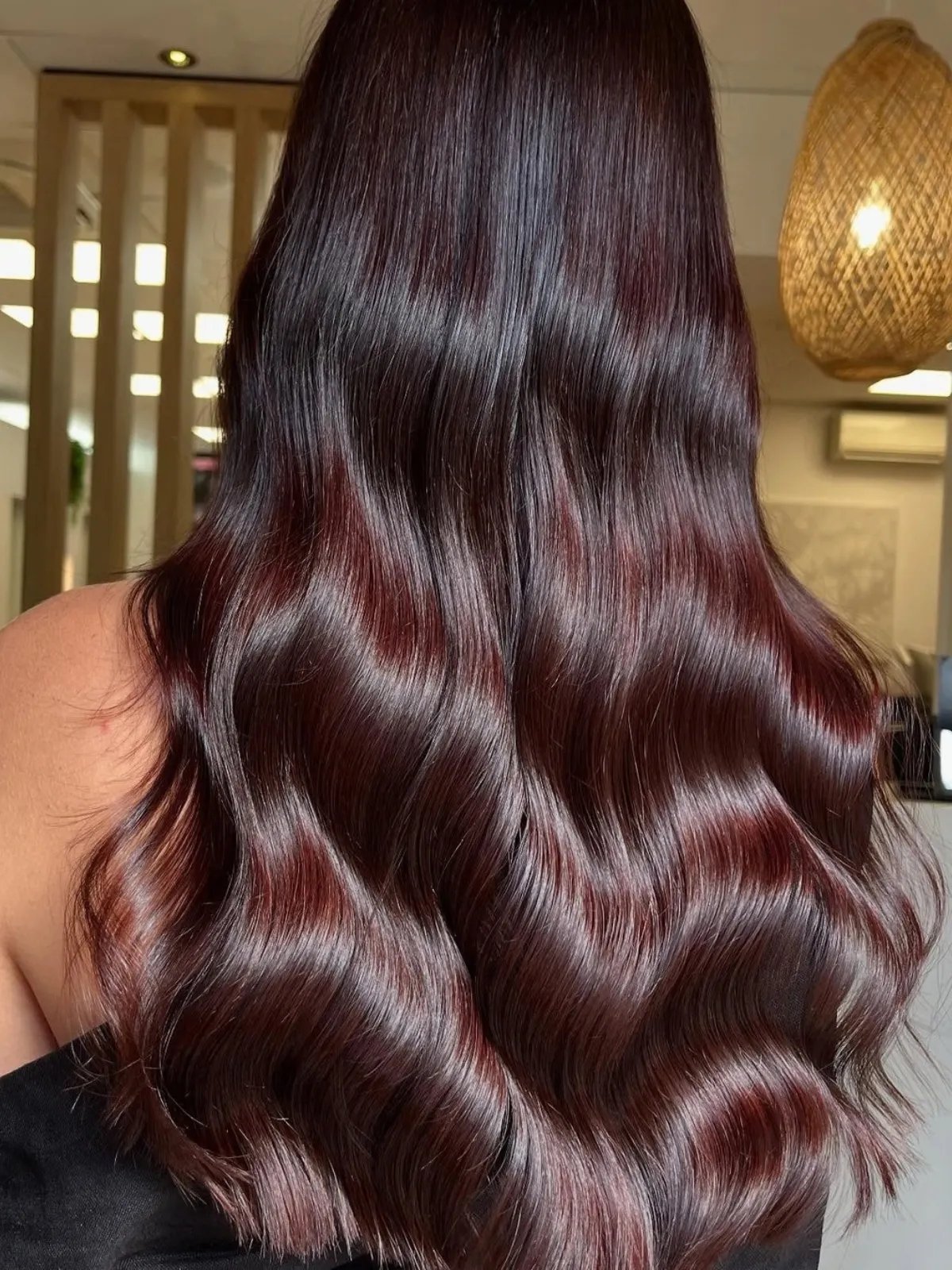 Model with long, loosely curled, glossy hair in a maroon red shade.