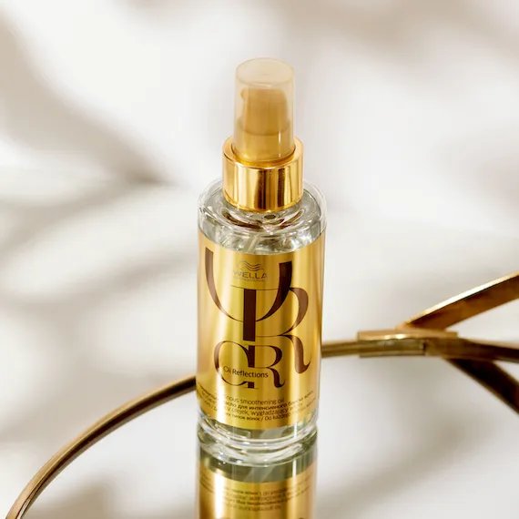 A bottle of Oil Reflections Luminous Smoothing Oil stands on a mirrored
surface.