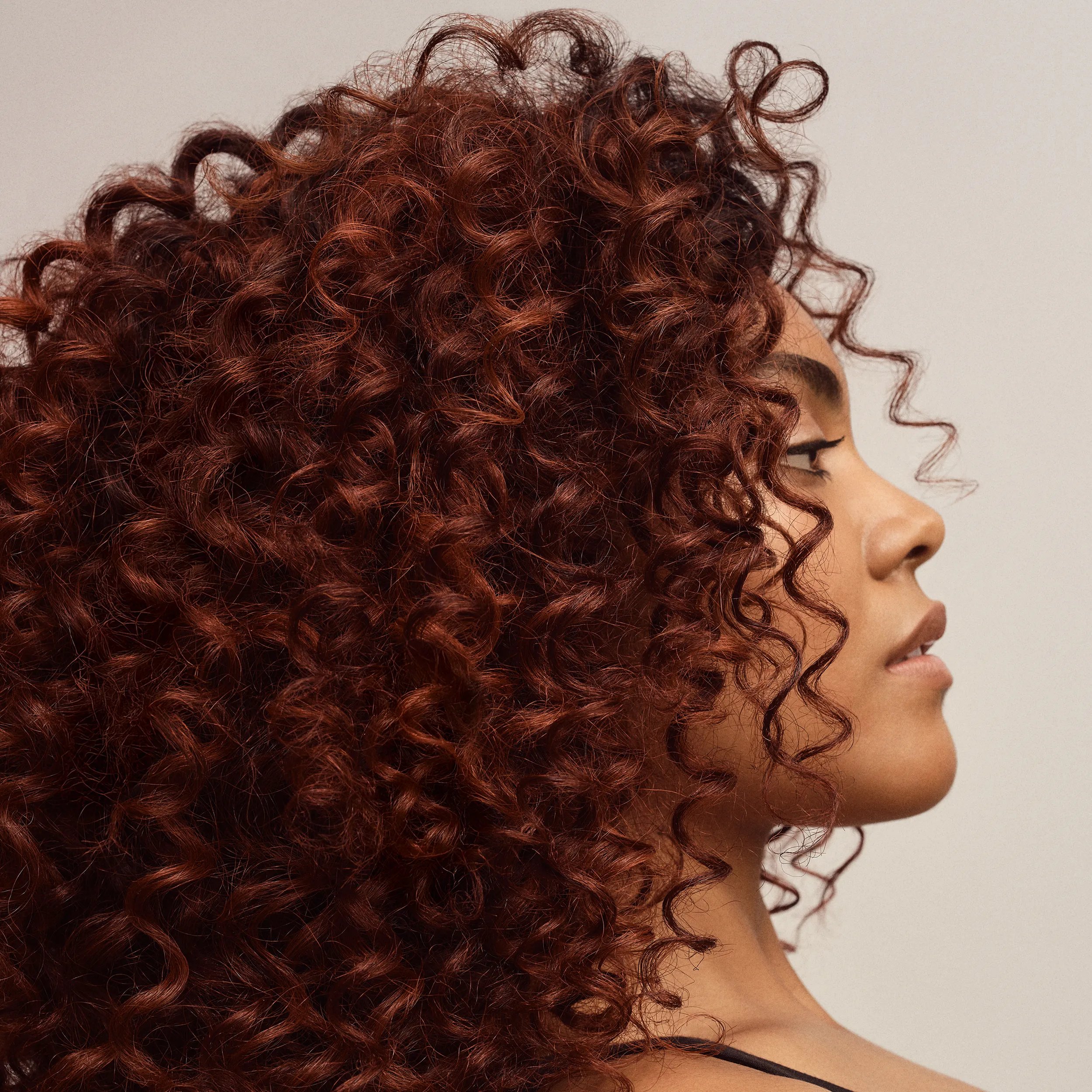 Woman with long brown curly hair looks at the camera