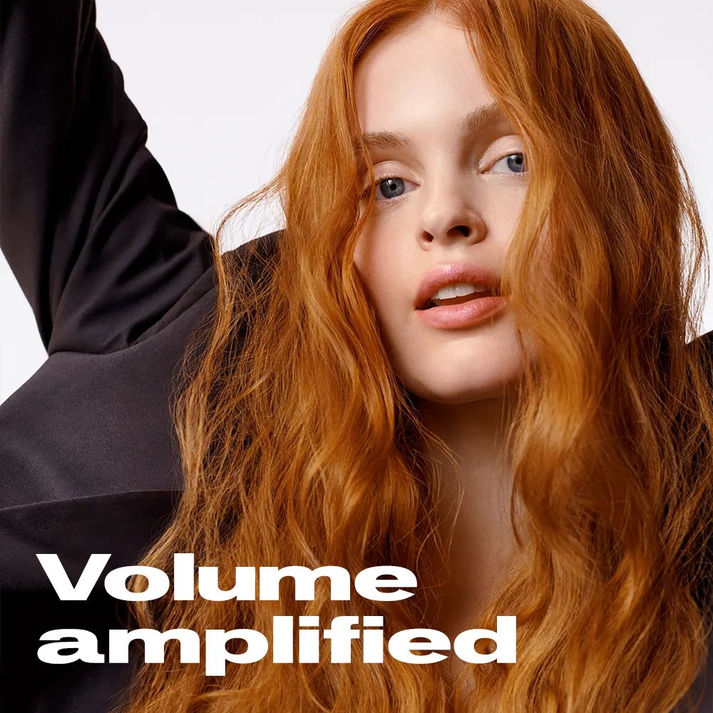 Model with wavy, auburn hair facing forward with arms raised. Text overlay states "Volume amplified"