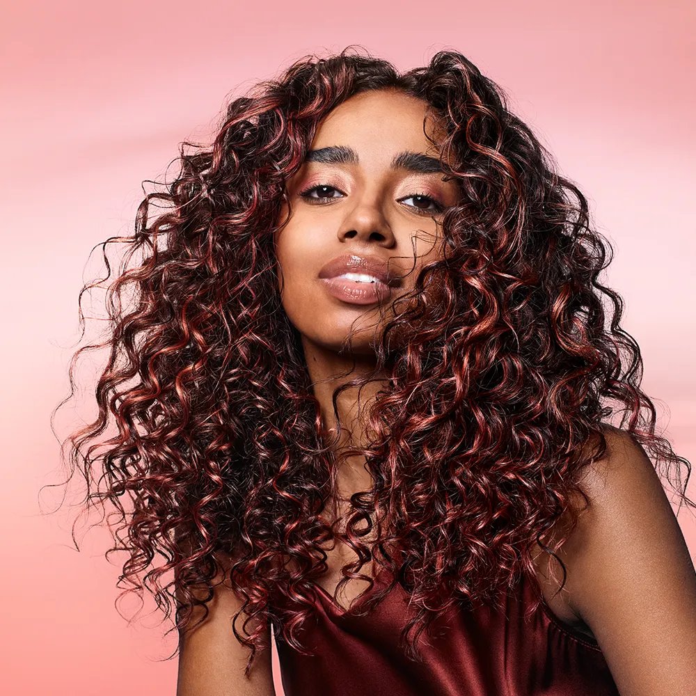 Model with long, dark, glossy, curly hair featuring coral highlights.