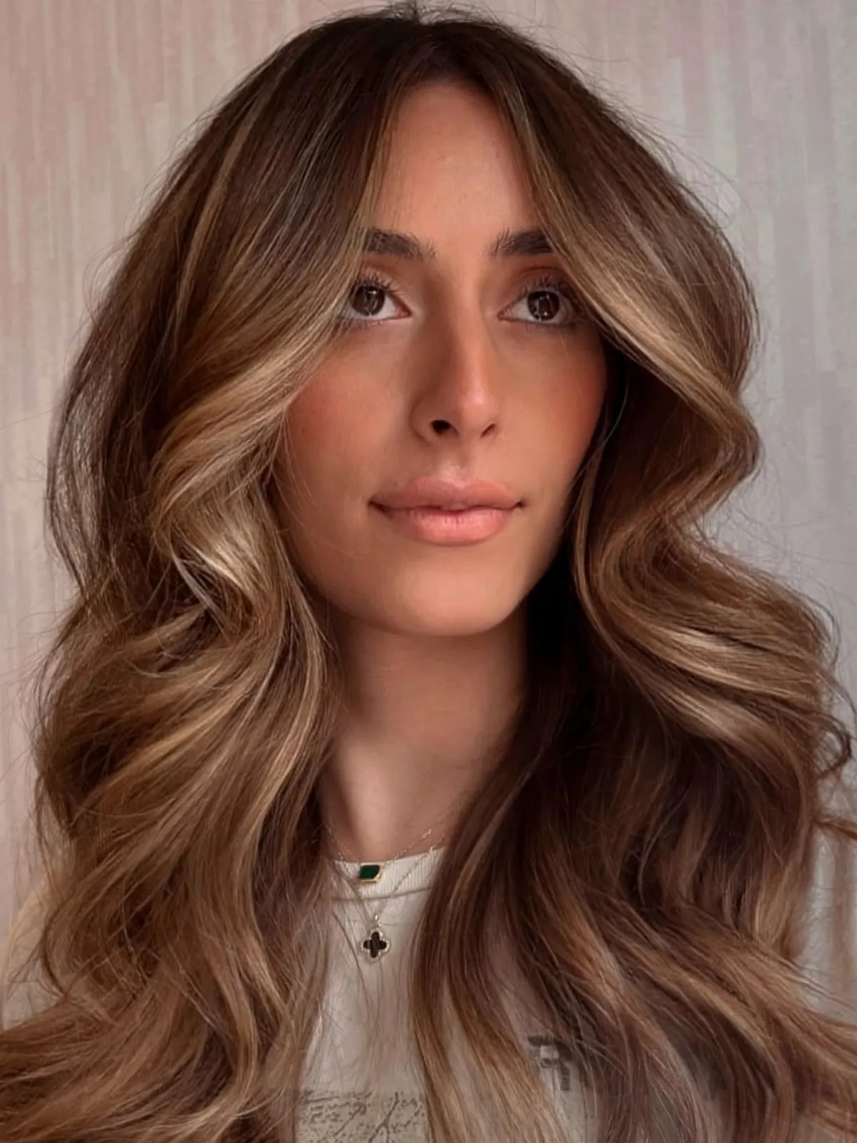 Model with voluminous, loosely curled, light brown hair and a sun-kissed balayage.