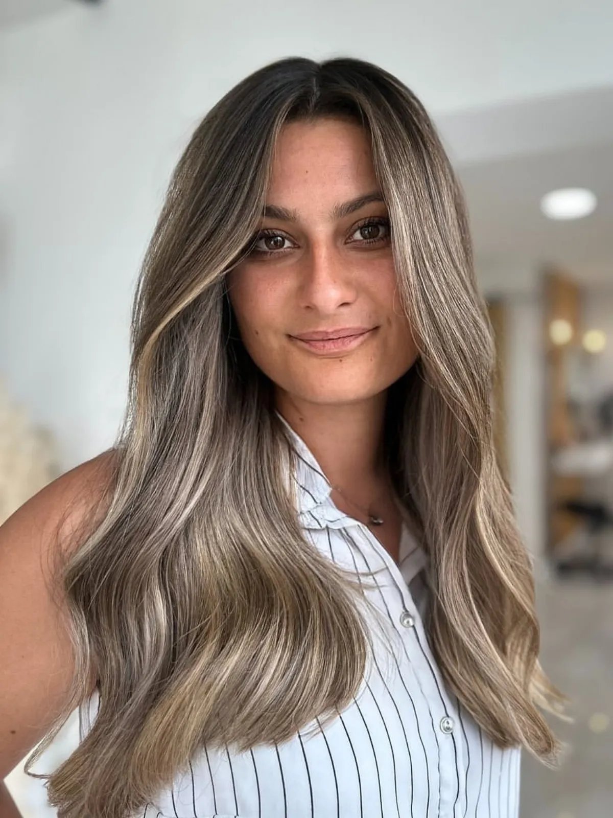 Model with long, loosely waved hair that’s dark at the roots with an ash blonde balayage.