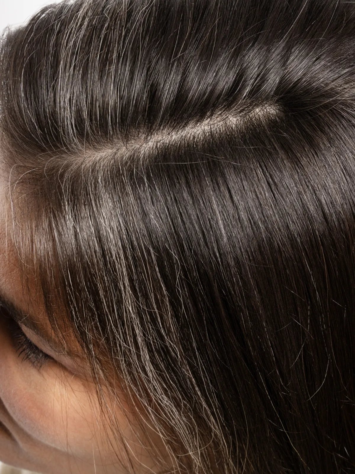 Close-up of model’s dark brown, straight hair with grey roots.