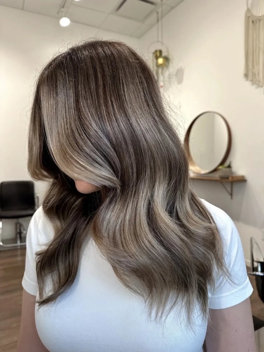 Model with long, wavy hair and cool-toned balayage highlights in a salon setting.