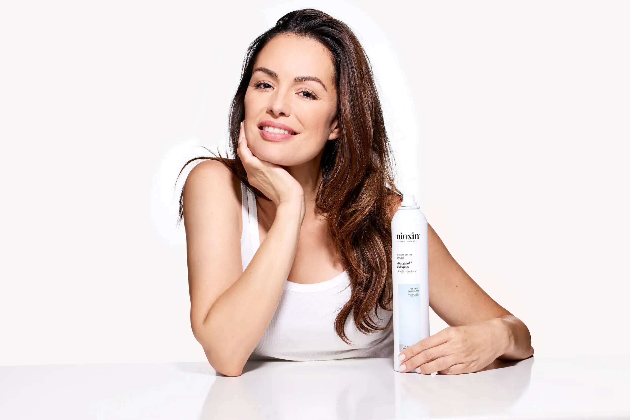 brunette woman resting head on palm holding Nioxin strong hold hairspray