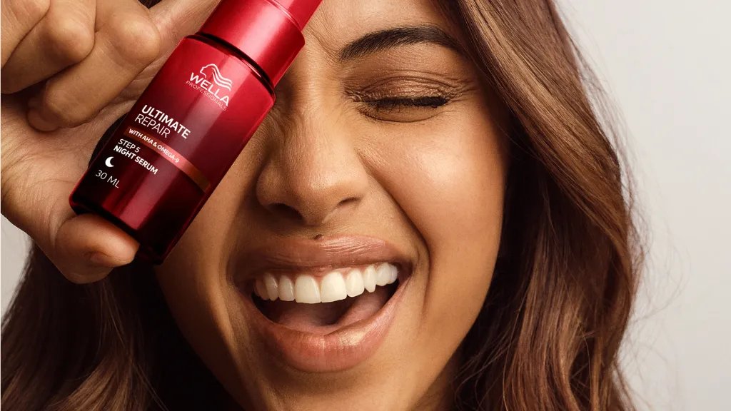 Model with long, brown, wavy hair holds a bottle of ULTIMATE REPAIR Night Serum.