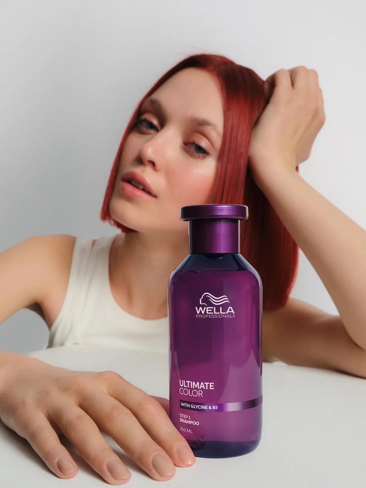 Model with red hair holds a bottle of ULTIMATE COLOR Shampoo.