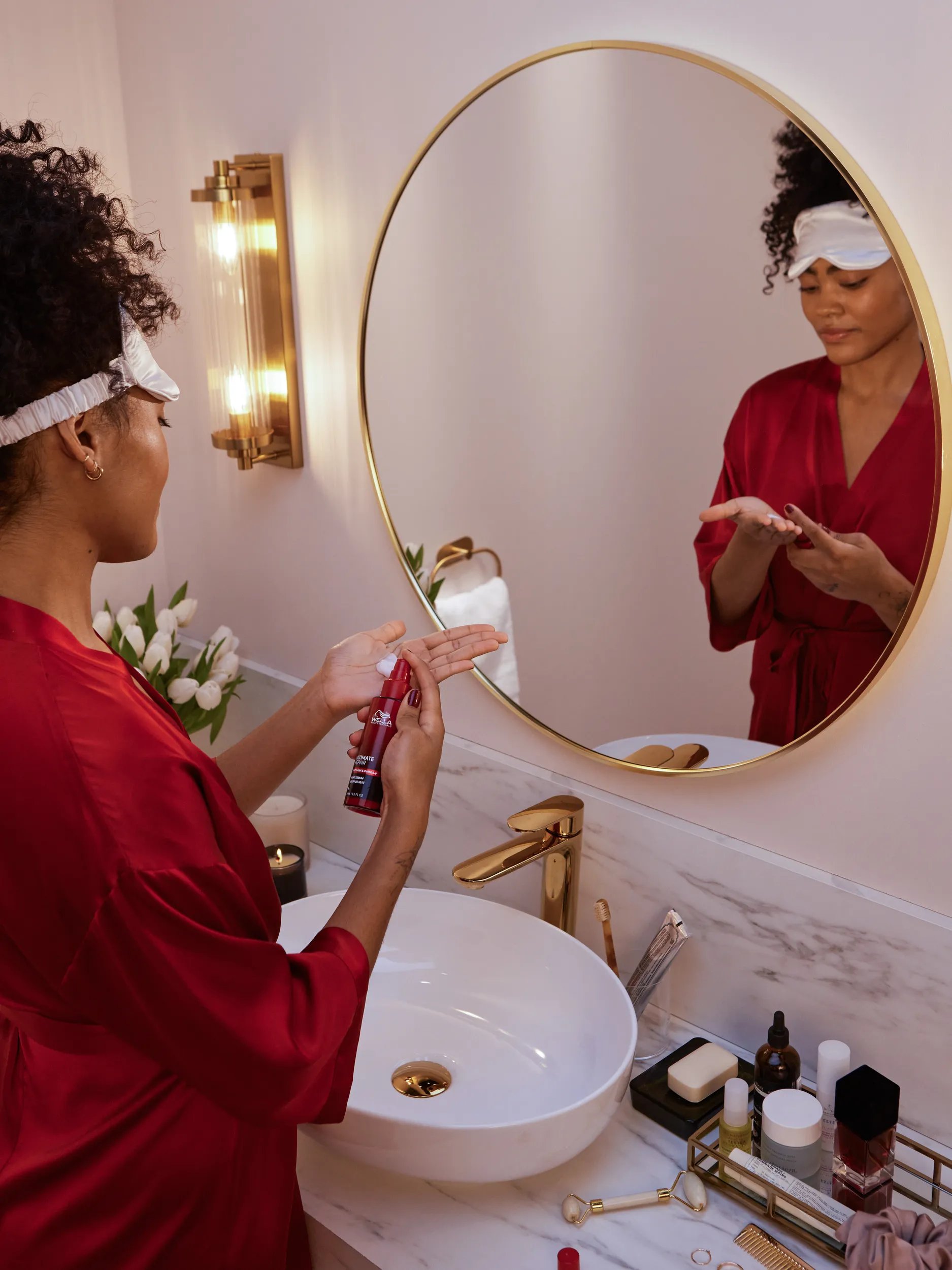 A model with dark, curly hair stands in front of the bathroom mirror and applies ULTIMATE REPAIR Night Serum. 