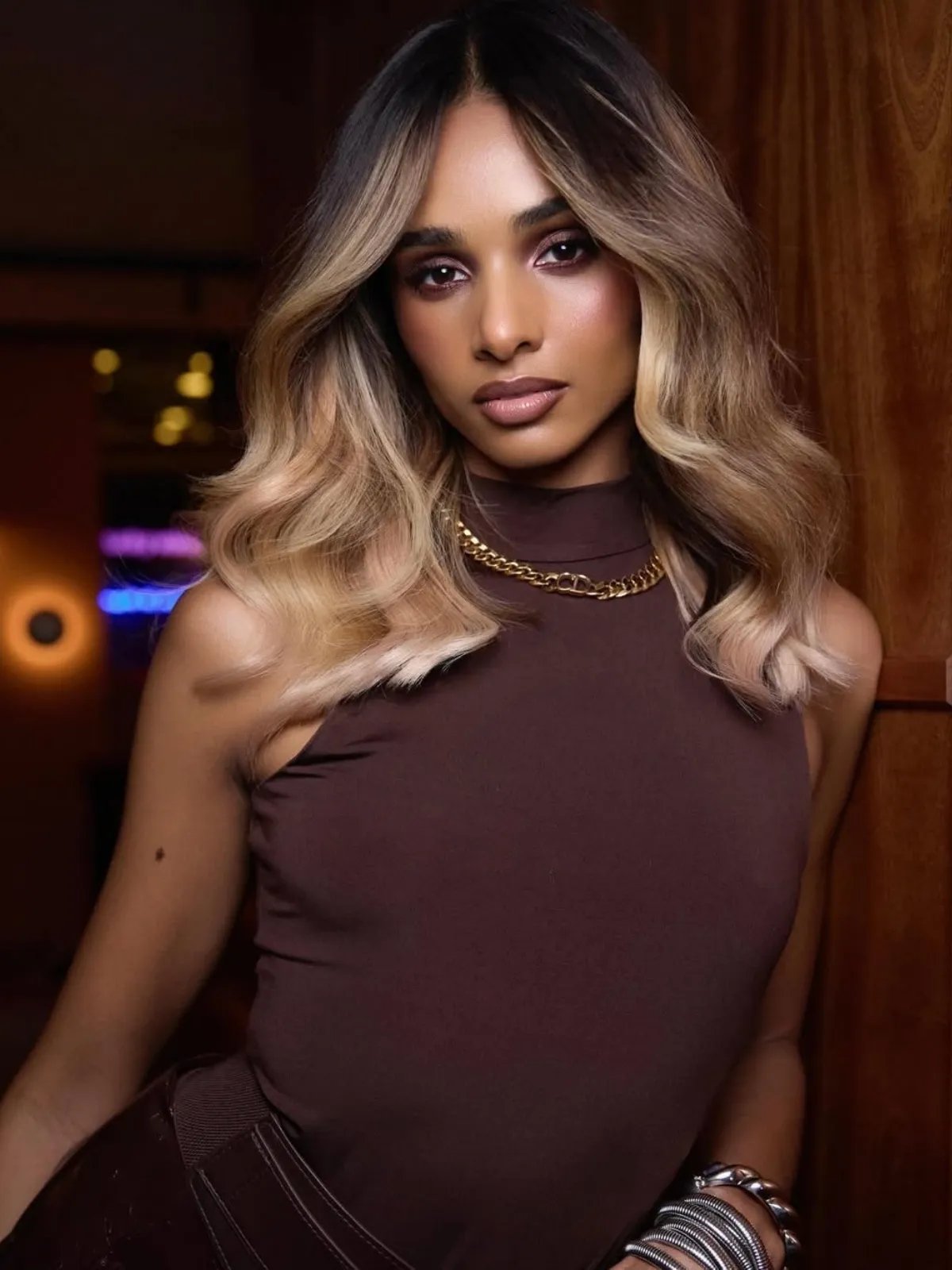 Model with loosely waved, glossy hair featuring dark roots and beige blonde lengths.