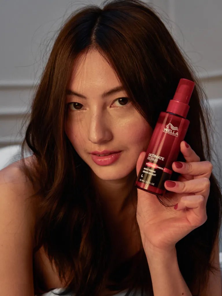 Model with dark brown hair holds up a bottle of ULTIMATE REPAIR Night Serum.