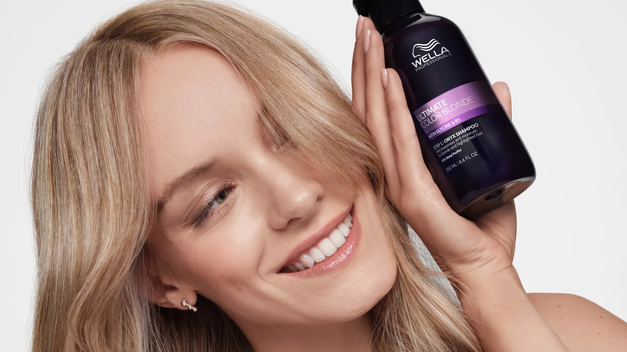 Blonde model holds a bottle of ULTIMATE COLOR BLONDE Onyx Shampoo.