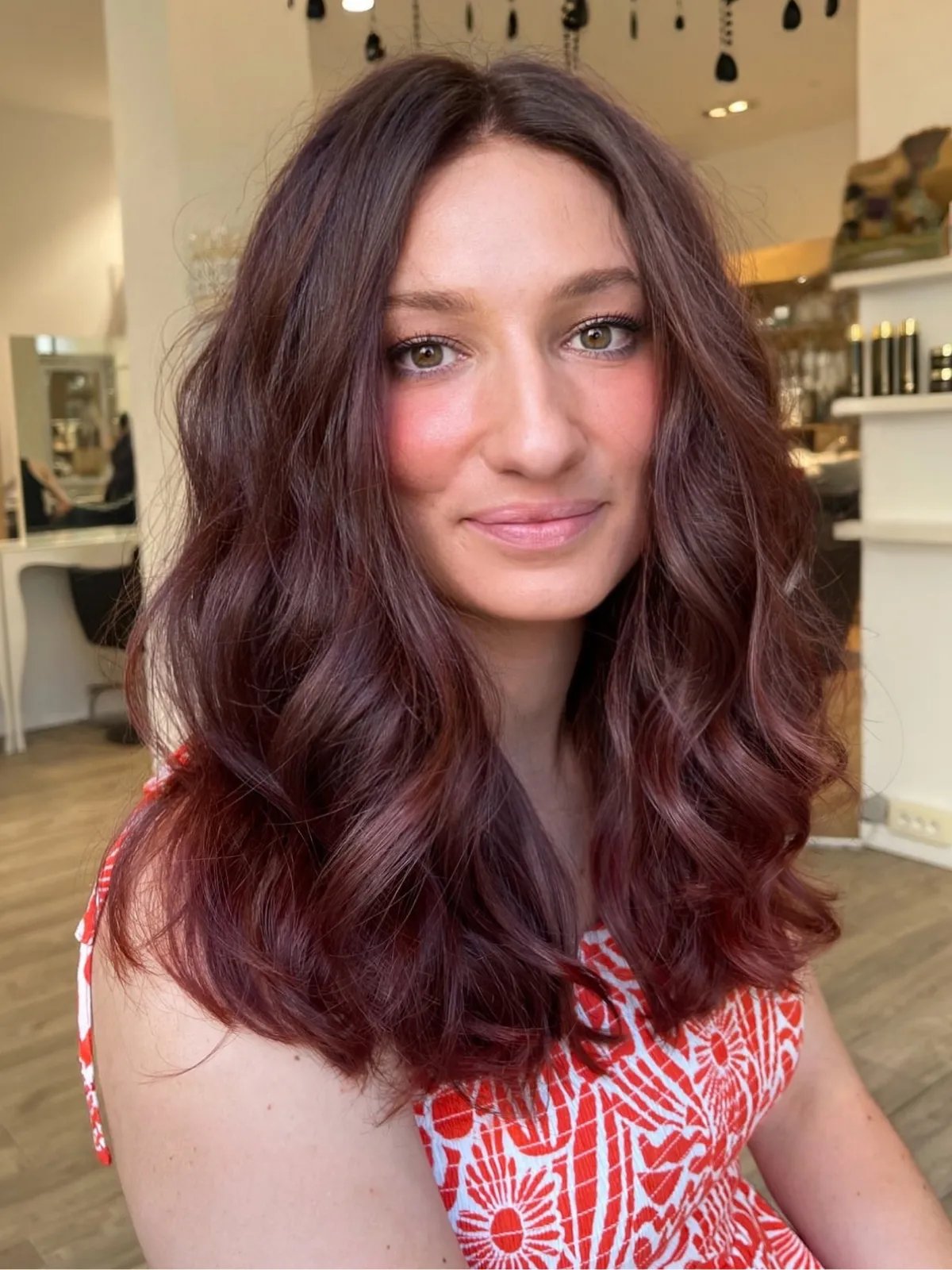 Model with loosely curled maroon hair featuring hints of plum through the ends.